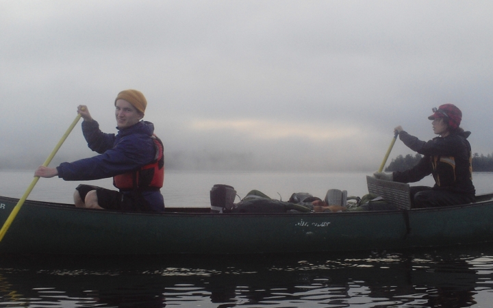two people paddle a canoe in fog with gray skies